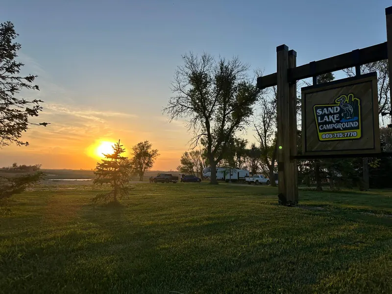 Sand Lake Campground sign at sunset with campers behind it