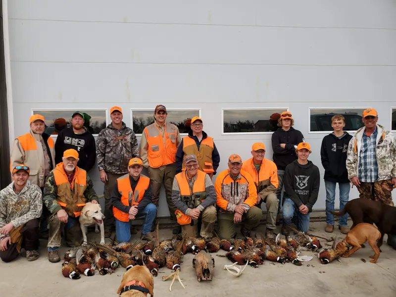 A group of pheasant hunters with their dogs and rows of roosters in front of the farm shop